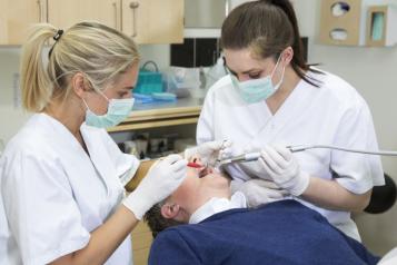 Two dentists conducting a procedure on a single patient in a clinical setting.