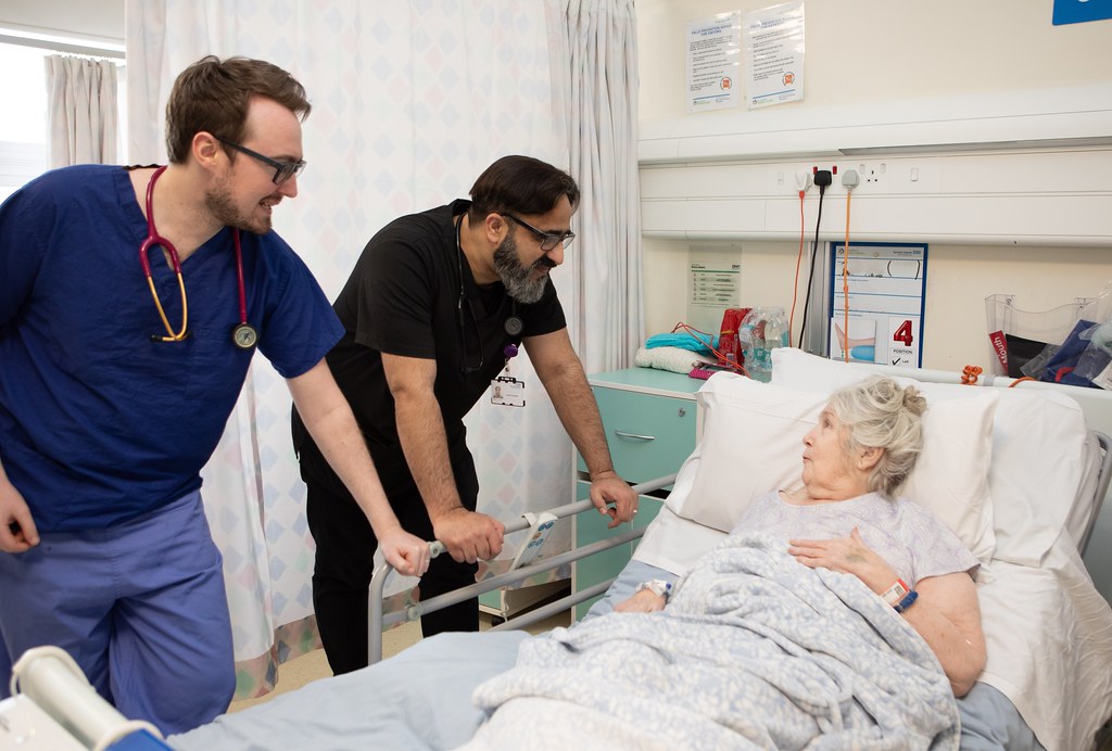 Woman in hospital receiving care at her bedside from two medical professionals