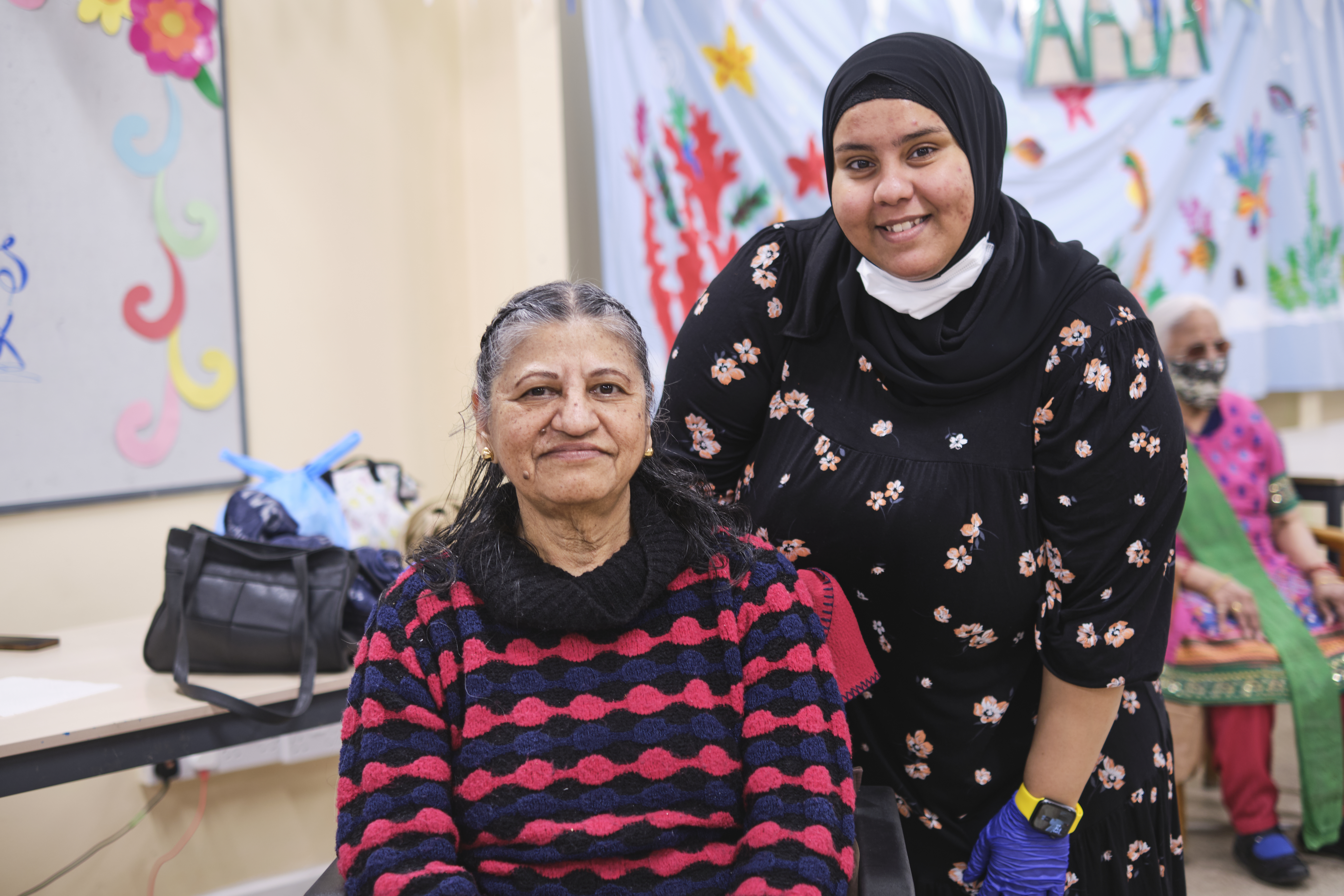 A young woman standing with an older woman sitting down.