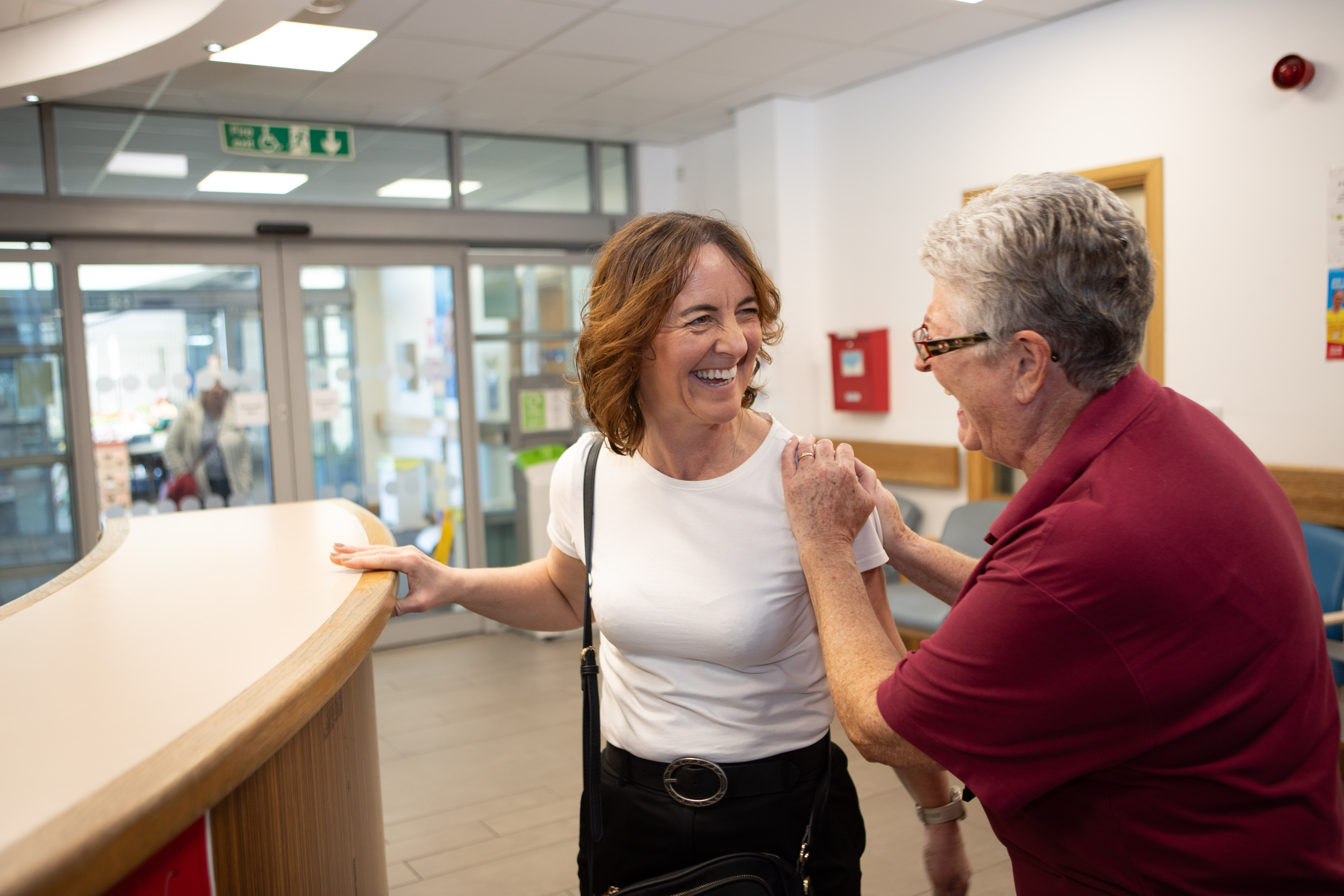 A woman and a volunteer laughing together in a hospital corridor.
