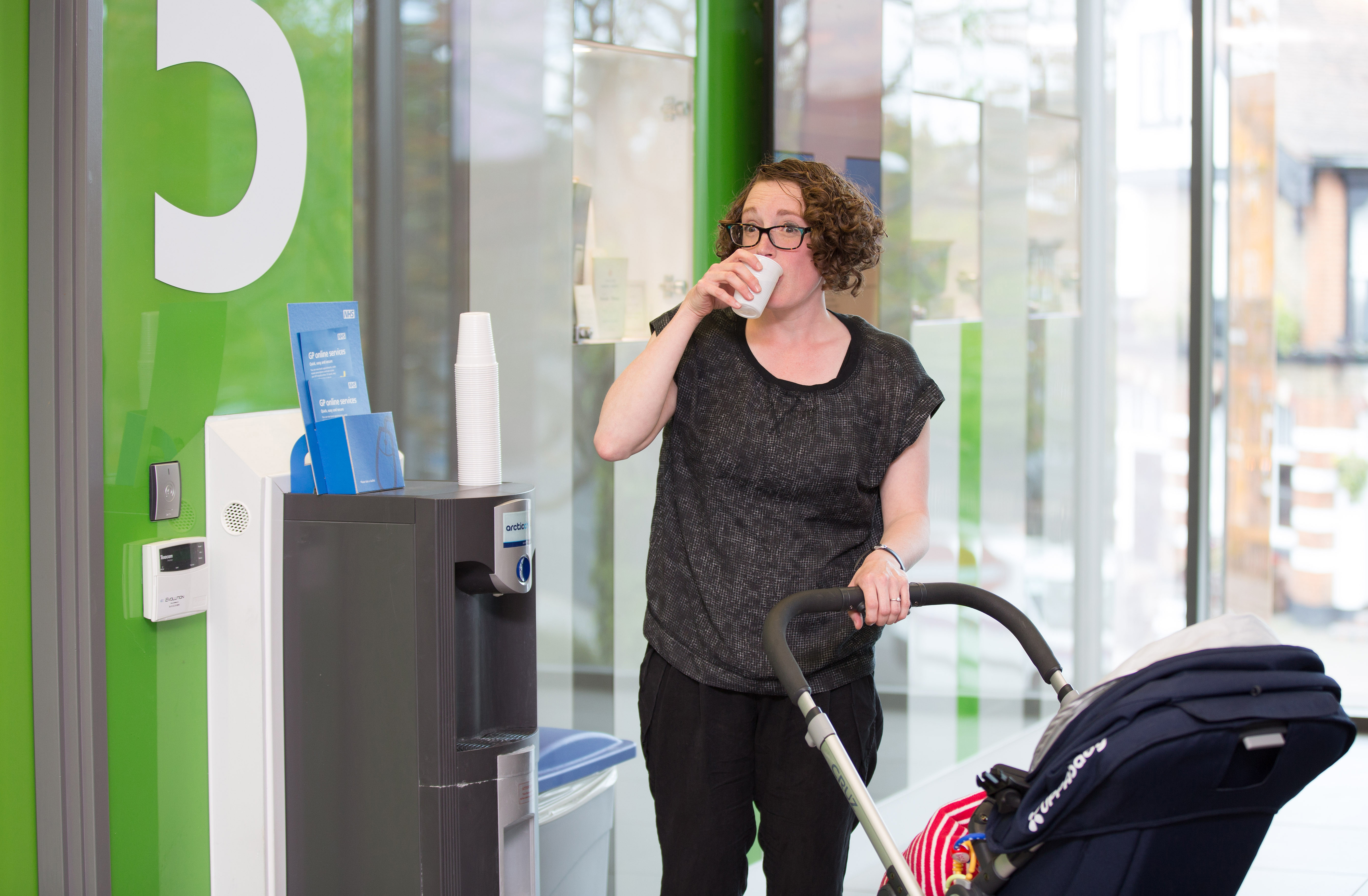 A woman with a pram drinking a cup of water in a clinical setting 
