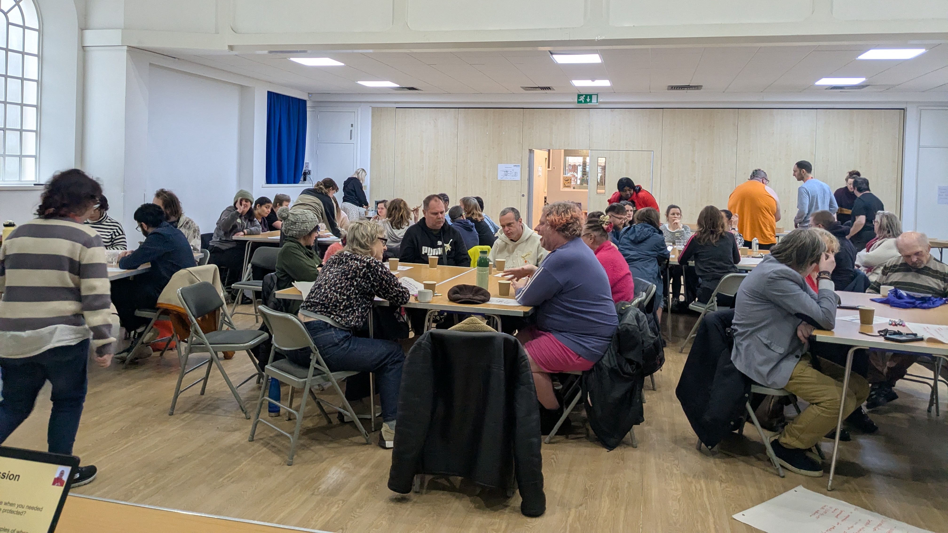A group of people sat at shared tables in a hall setting.