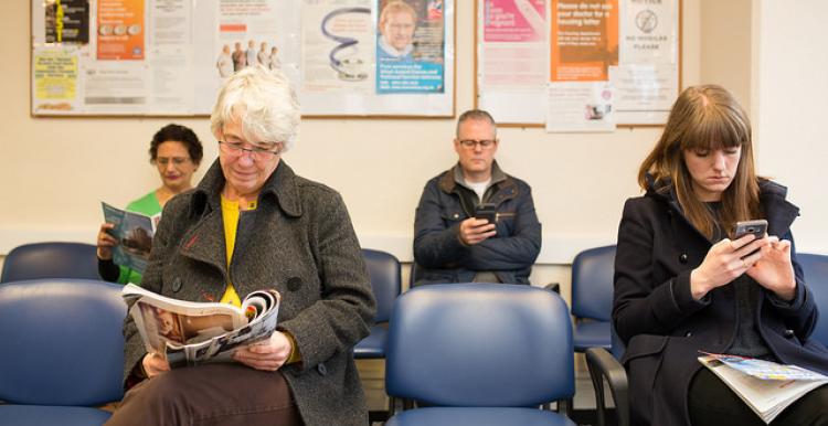 Four people sat in a waiting room reading or looking at their phones.