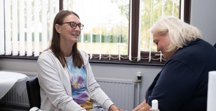 Two women sat down and holding hands in a supportive way.