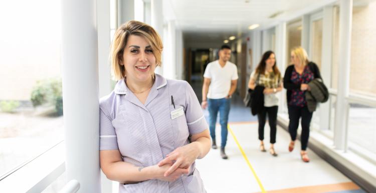 Medical professional standing in corridor with three people walking behind them.