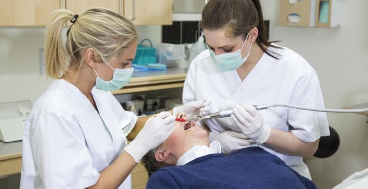Two dentists conducting a procedure on a single patient in a clinical setting.
