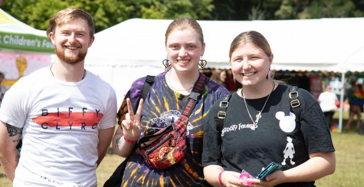 Three young people outside in a sunny, festival environment.