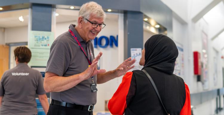 A volunteer speaking to a service user in the corridor of a hospital.