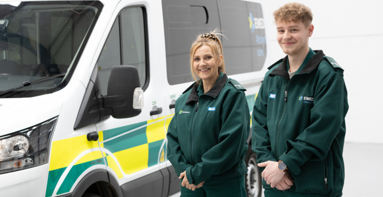An ambulance with two medical professionals smiling in front of it.