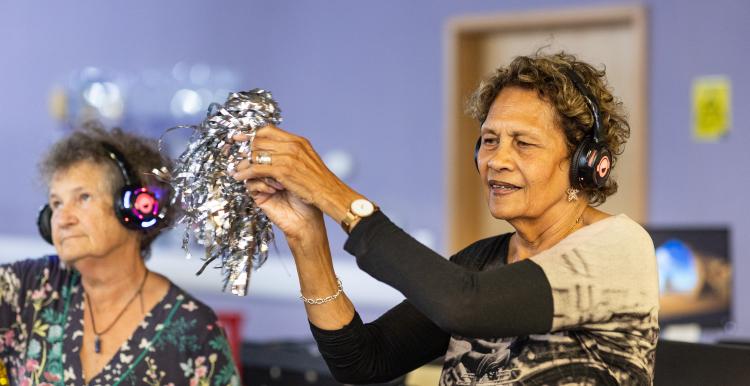 Two older women taking part in a creative dance exercise indoors.