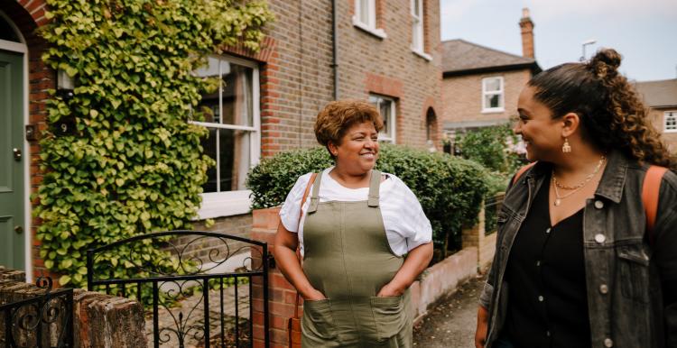 Two women walking together and smiling outside terraced houses.