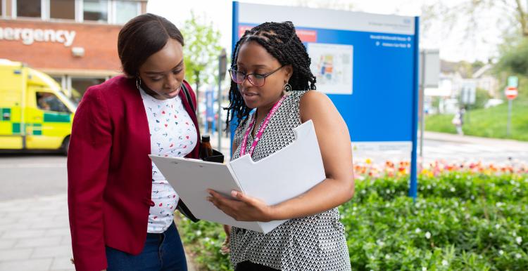 Two women looking at a folder outside a hospital.