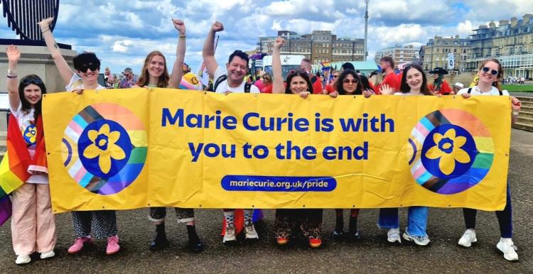 A group photo of a team of Marie Curie employees with a Pride banner and flags.