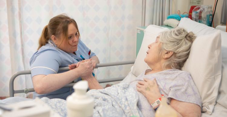 Older woman receiving bedside care in hospital.