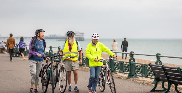 Three people with bikes walking along Brighton seafront.