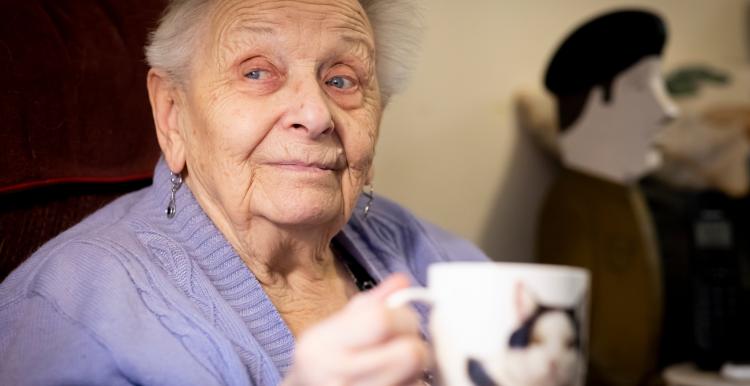 An older woman holding a mug with a cat on it.