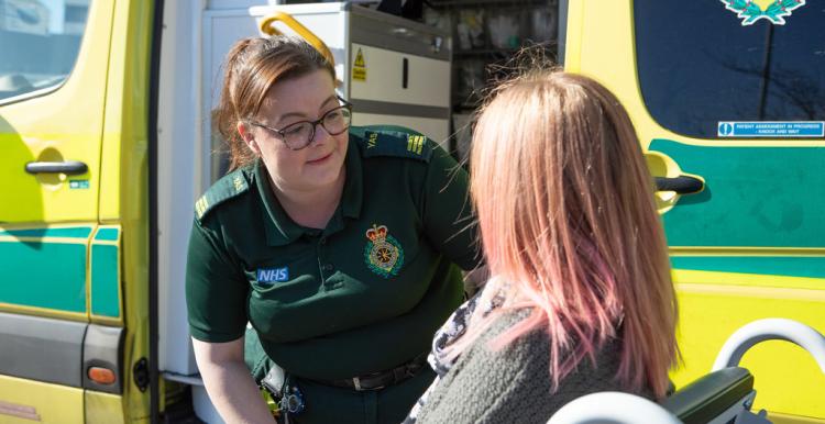 An ambulance professional talking to a service user in front of an ambulance.