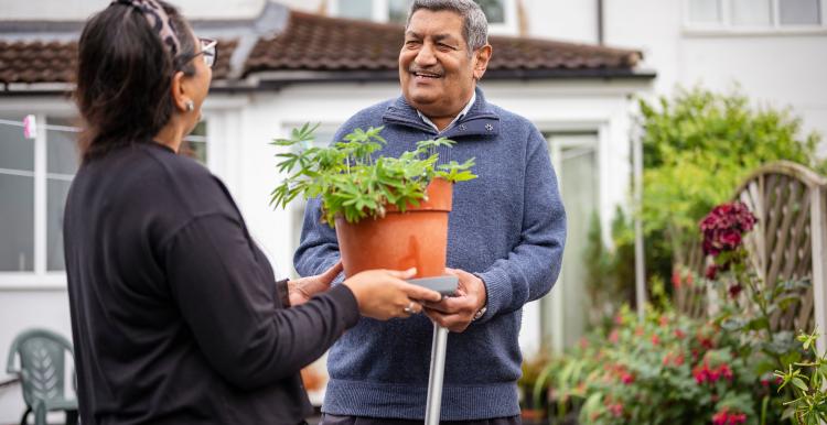 Older man receiving a potted plant from a woman in a garden.