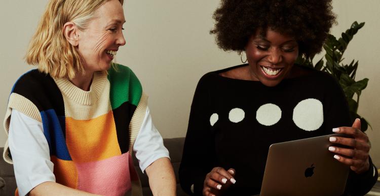 Two women looking at a computer and laughing on a sofa
