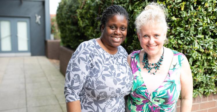 Two women smiling together outside a building.