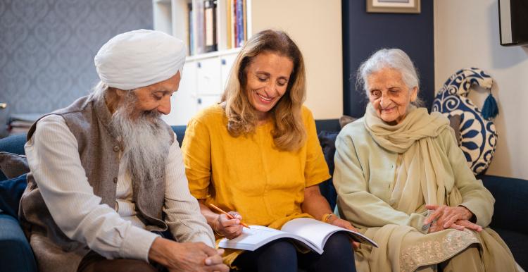 Three older adults smiling together indoors looking at a document