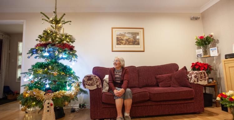 Older woman sat on sofa looking at Christmas tree