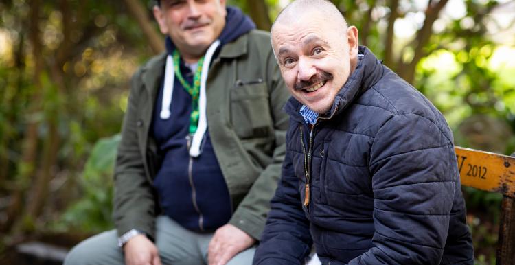 Two men sat outside smiling together.