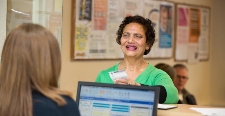 Woman talking at a GP reception counter.