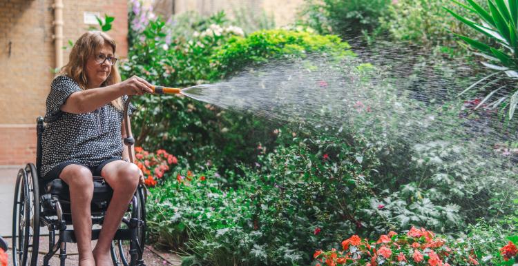 Woman in a wheelchair watering a garden.