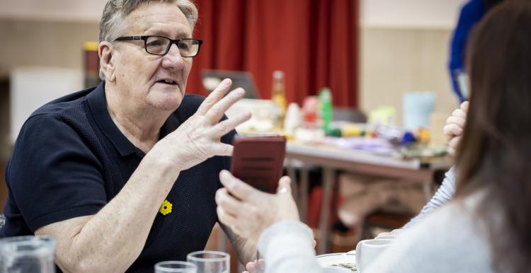 Man talking while someone shows him a phone.