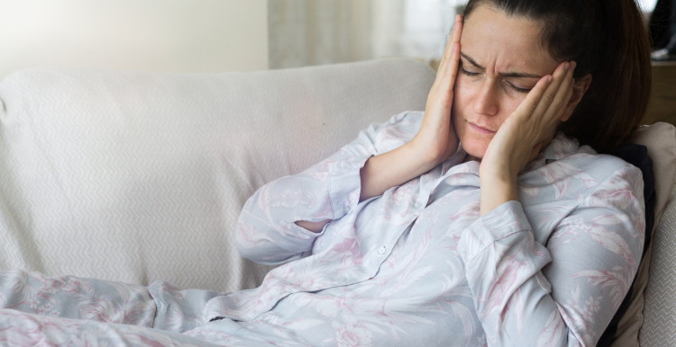 Woman lying on sofa and holding head as if in pain.