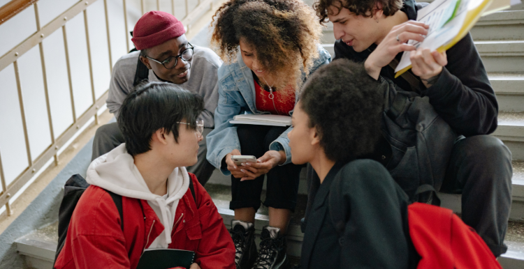 A group of young people sat together on a staircase looking at a phone.