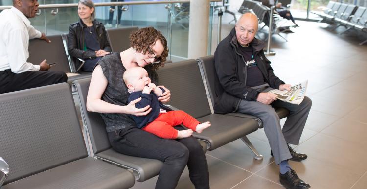 Several people in a clinical waiting room with one woman with a baby on her lap.