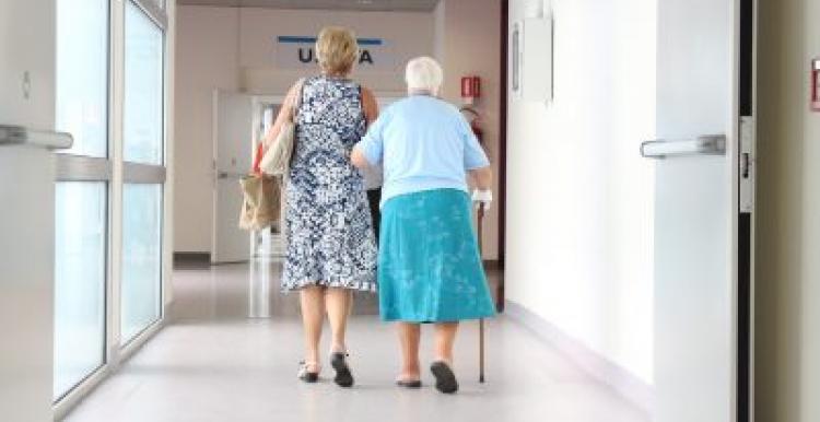 Hospital corridor, Old woman walking arm in arm with a woman, backs to camera