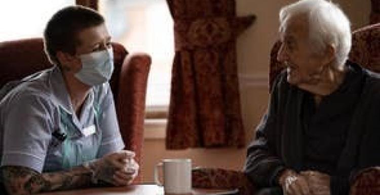 A masked carer talking to an older person 