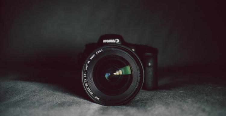 Black backdrop, Canon camera centrally framed, Lens in focus, Background blurred