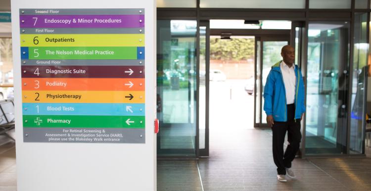 Man standing in hospital next to signage.