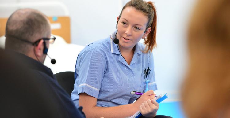 Female nurse, facing towards patient, patient out of focus and at forefront of image