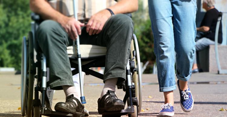 Close up from shoulders down, man in wheelchair to left, someone walking alongside