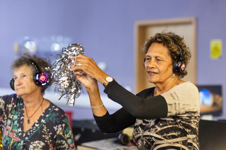 Two older women taking part in a creative dance exercise indoors.