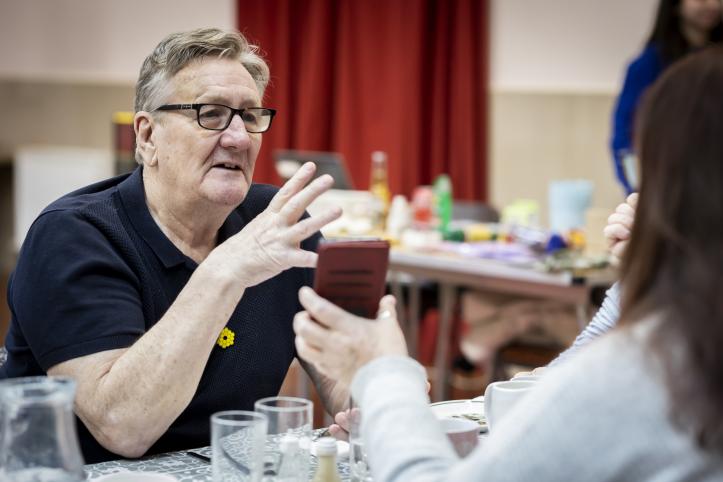 Man talking while someone shows him a phone.