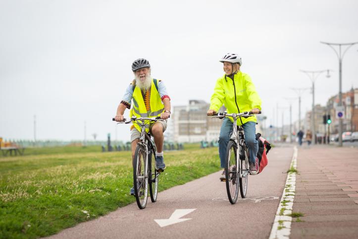 Two older adults cycling together along Brighton seafront.