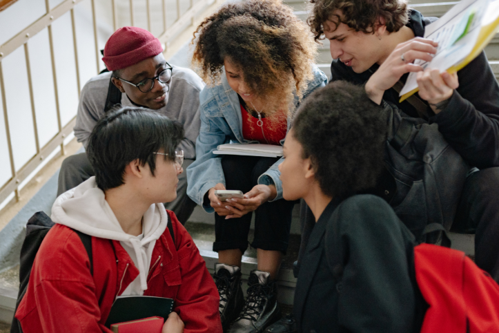 A group of young people sat together on a staircase looking at a phone.