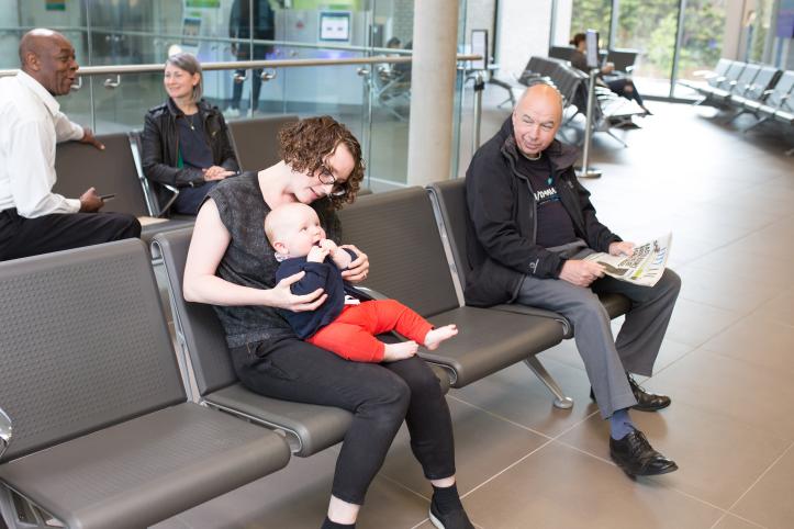 Several people in a clinical waiting room with one woman with a baby on her lap.