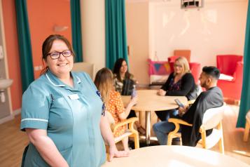 Care worker standing next to table of people sitting.