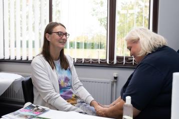 Two women sat down and holding hands in a supportive way.