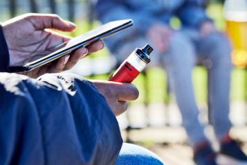 Young person vaping outside with one other young person.