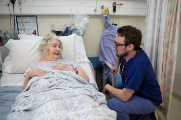 Older woman in hospital bed receiving care from a male doctor. 