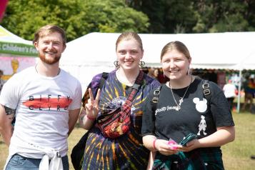 Three young people outside in a sunny, festival environment.
