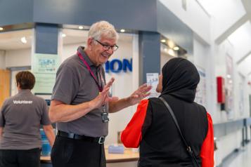A volunteer speaking to a service user in the corridor of a hospital.